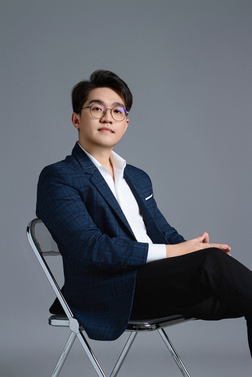 Young man in elegant attire sitting indoors, exuding confidence and sophistication.